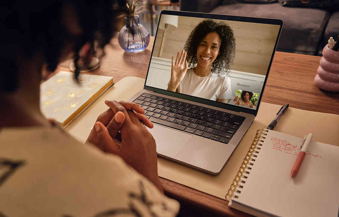 woman looking at laptop screen with another woman waving