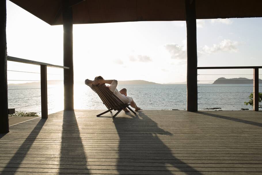 A man relaxes on a beach chair by the sea, lying back with his hands behind his head.