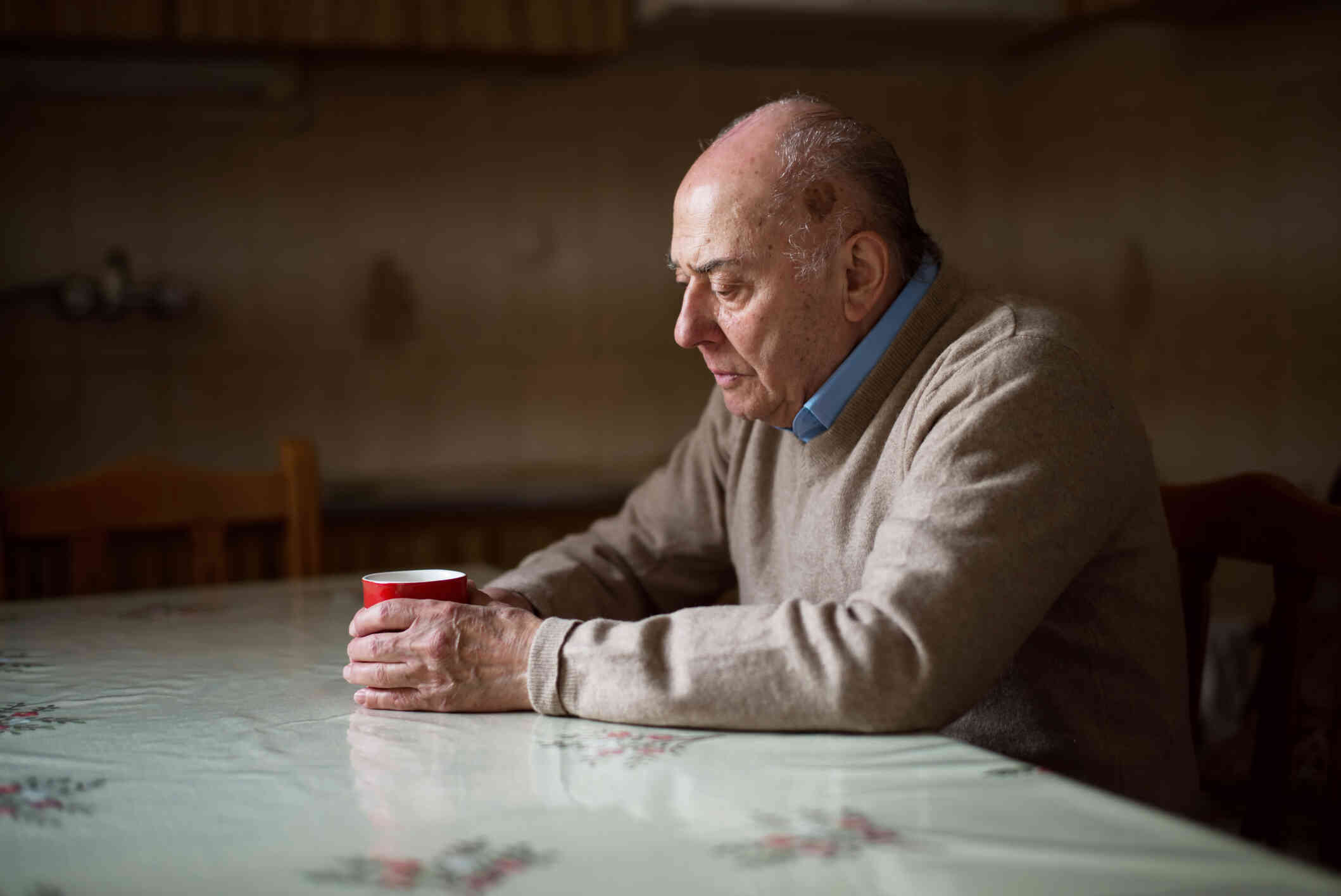 An elderly man seated at a table a holding a red cup